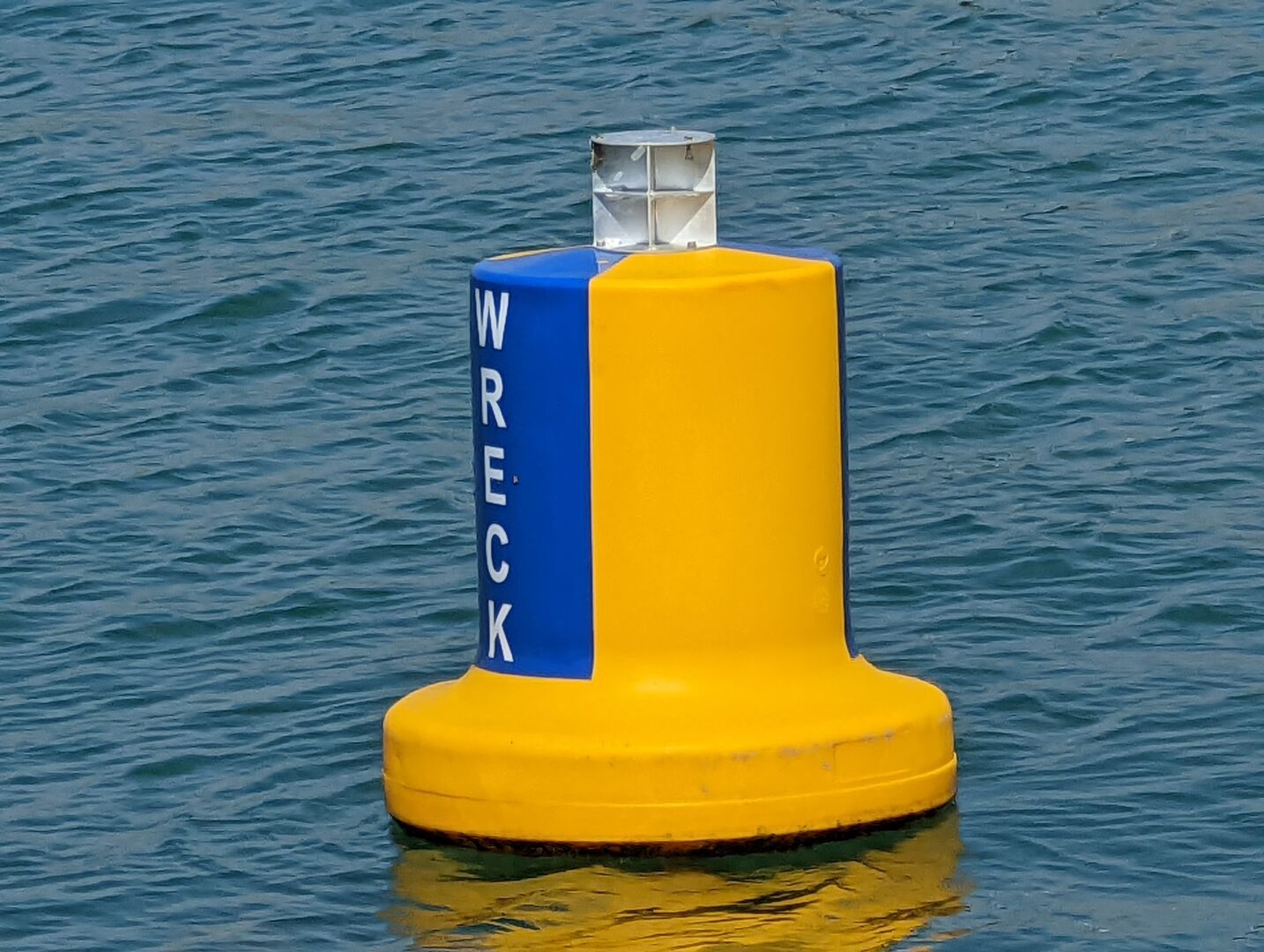 Yellow buoy with white radar reflector beacon on top, floating in aquamarine water and with a navy blue flash down the side stating WRECK in white letters